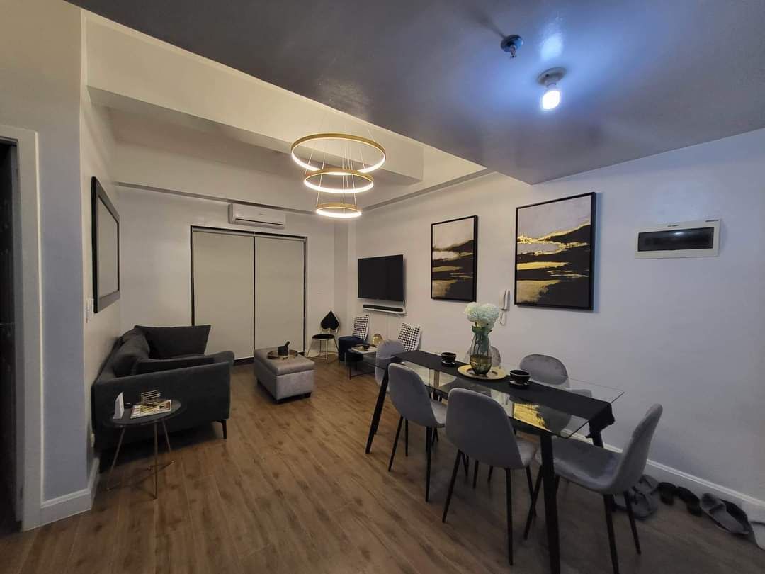 A modern living room with a sofa, dining table, and chairs. There is a ceiling light fixture and artwork on the walls.