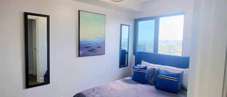 A bedroom with a large bed, a ceiling light fixture, a window with a view, and a painting on the wall.