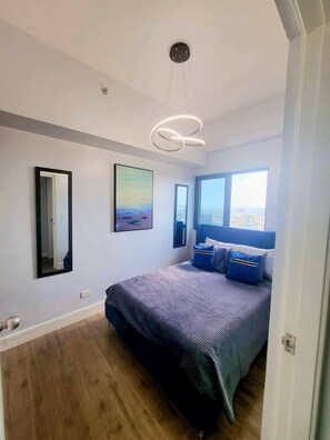 Een slaapkamer met een groot bed, een plafondlamp, een raam met uitzicht en een schilderij aan de muur.