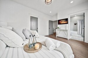 Quarto de hotel moderno com cama, televisão, banheiro e corredor.
