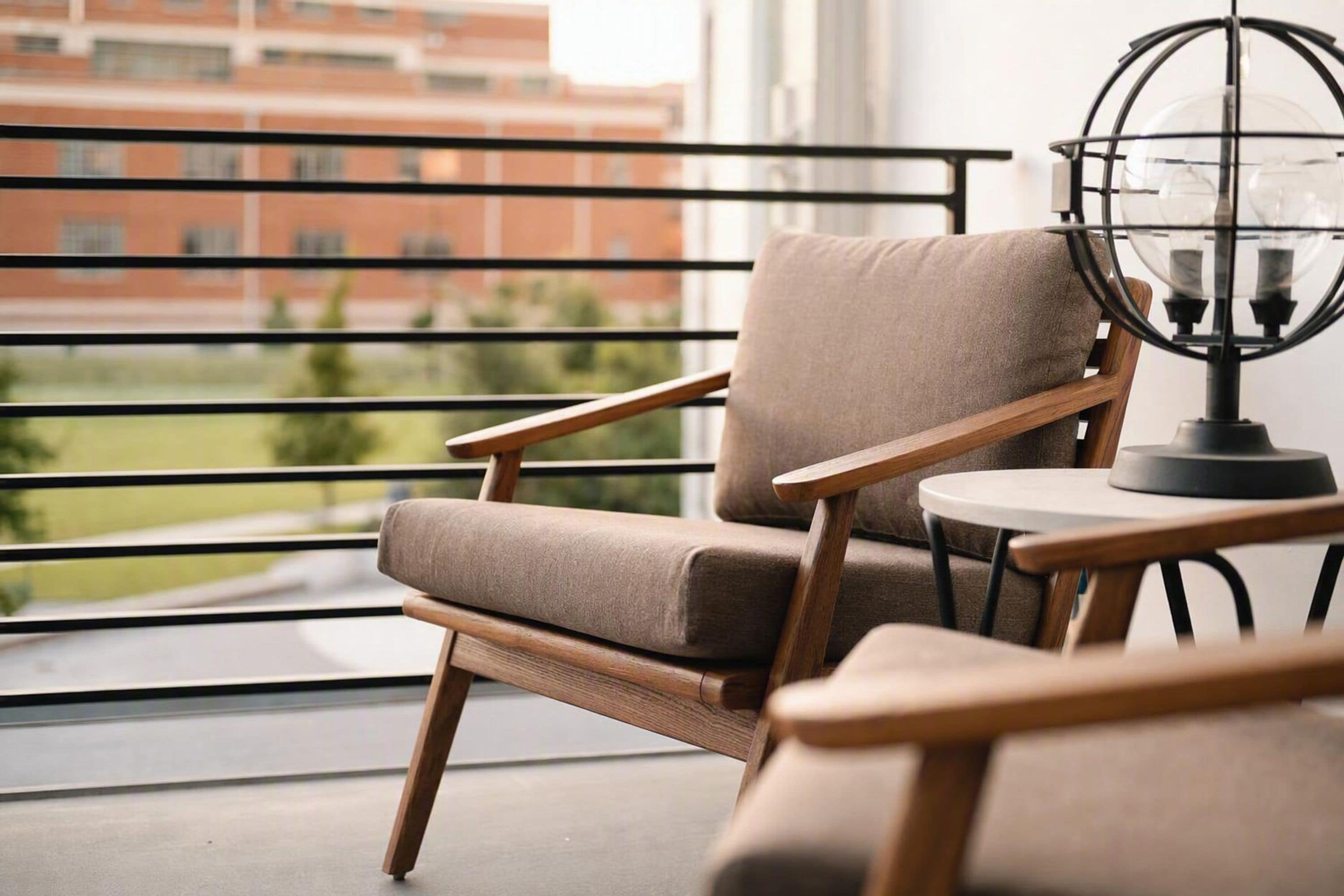 Un fauteuil moderne, doté d’un siège rembourré et d’une structure en bois, placé près d’une fenêtre offrant une vue sur un bâtiment et de la verdure.
