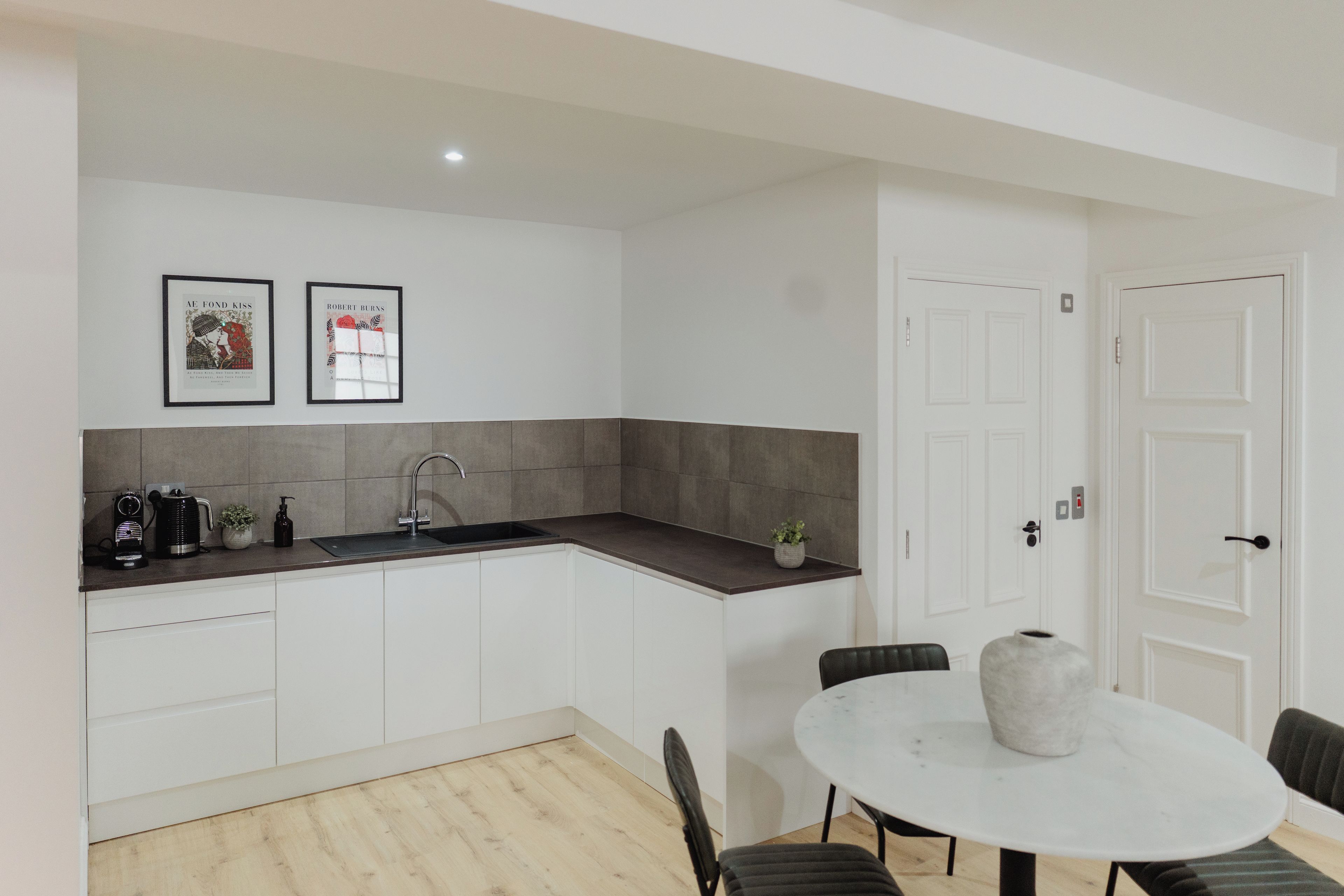 A modern kitchen with a dark countertop, white cabinets, and a sink. There are two framed artworks above the counter.