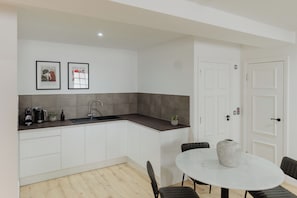 A modern kitchen with a dark countertop, white cabinets, and a sink. There are two framed artworks above the counter. - Joivy Vaults Studios & Apartments (Edinburgh)