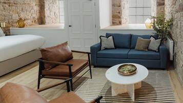 A modern living room with a sofa, armchair, and coffee table, featuring stone walls and a view through a window.
