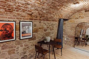 Un intérieur aux murs de pierre, avec une table et des chaises, des affiches encadrées accrochées au mur et un luminaire suspendu.