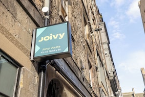 A sign for Joivy Vaults on a building with a stone facade and visible pipes. - Joivy Vaults Studios & Apartments (Edinburgh)