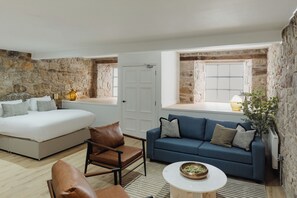 Une chambre à coucher avec un lit, un canapé bleu, un fauteuil en cuir marron et une petite table sur laquelle se trouve un bol.