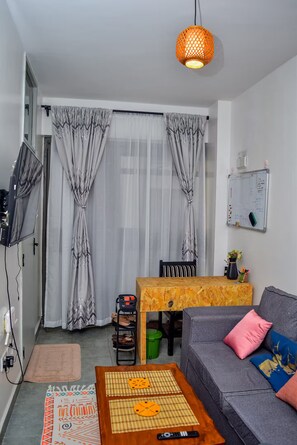 A living room with a sofa, a wooden coffee table, a TV, a whiteboard, and a hanging lamp. - The Sunset Nest - Serene 1-bedroom apartment perfect for relaxing stay (Kiambu Province)