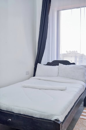 A neatly made bed with white bedding and a dark headboard, positioned in a room with a large window and sheer curtains. - The Sunset Nest - Serene 1-bedroom apartment perfect for relaxing stay (Kiambu Province)