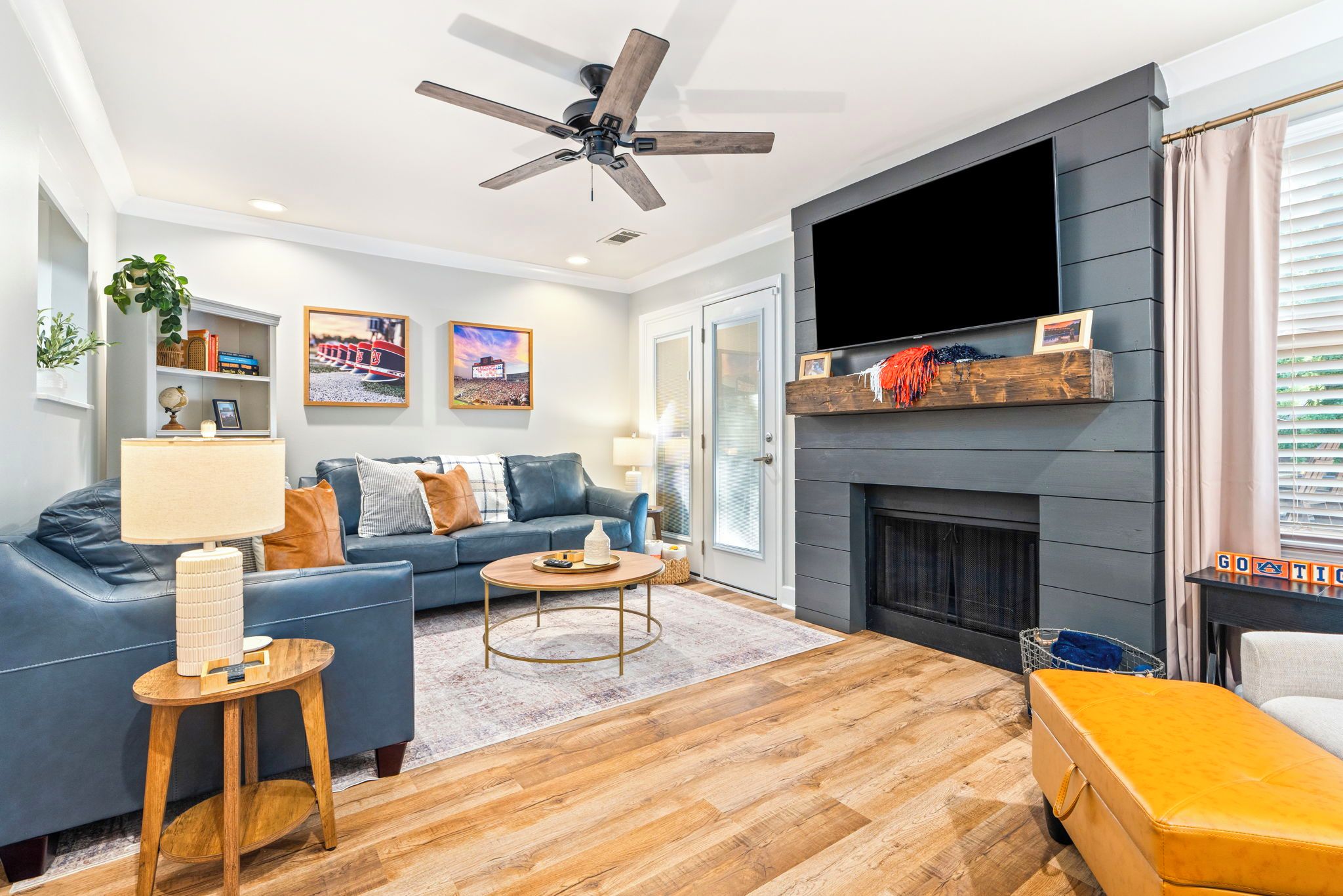 A modern living room with a blue sofa, a round coffee table, a fireplace, and a ceiling fan.