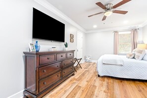 Ein Schlafzimmer mit einem großen Bett, einem Schminktisch, einem Deckenventilator und einem Fernseher an der Wand.