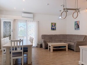 Ein Wohnzimmer mit einer Couch, einem Esstisch mit Stühlen, einer Hängeleuchte und zwei Wandbildern.