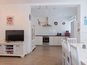 Eine moderne Küche mit weißen Schränken, einem eingebauten Backofen und einem Essbereich mit einem weißen Tisch und Stühlen.