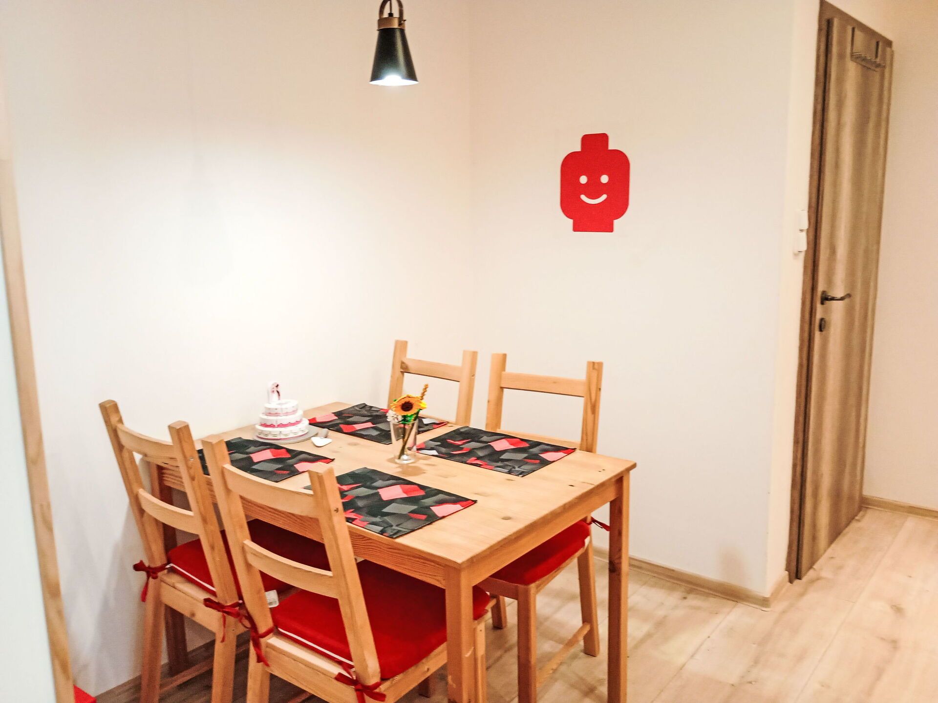 Un comedor con una mesa y sillas de madera, un pastel y un jarrón con un girasol.