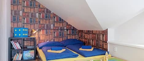 A bedroom with a sloped ceiling, a bed with blue bedding, a bookshelf, and a small table with a green surface.