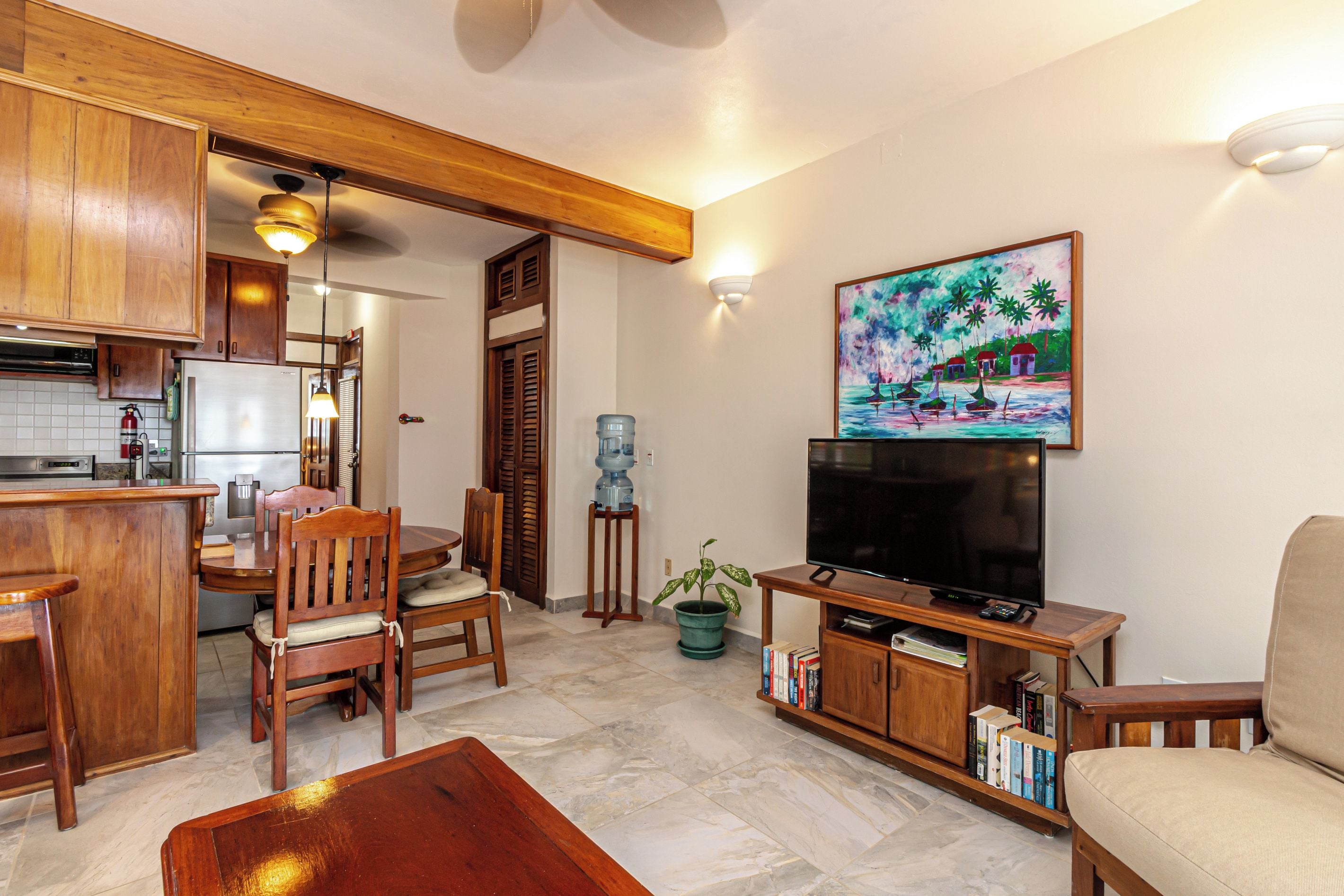A living room with a television, wooden furniture, a water dispenser, and a painting on the wall.