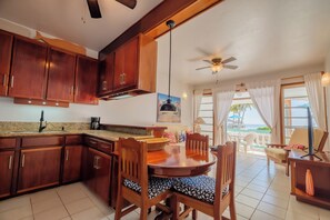 Een keuken met houten kastjes, een eettafel met stoelen en een plafondventilator.