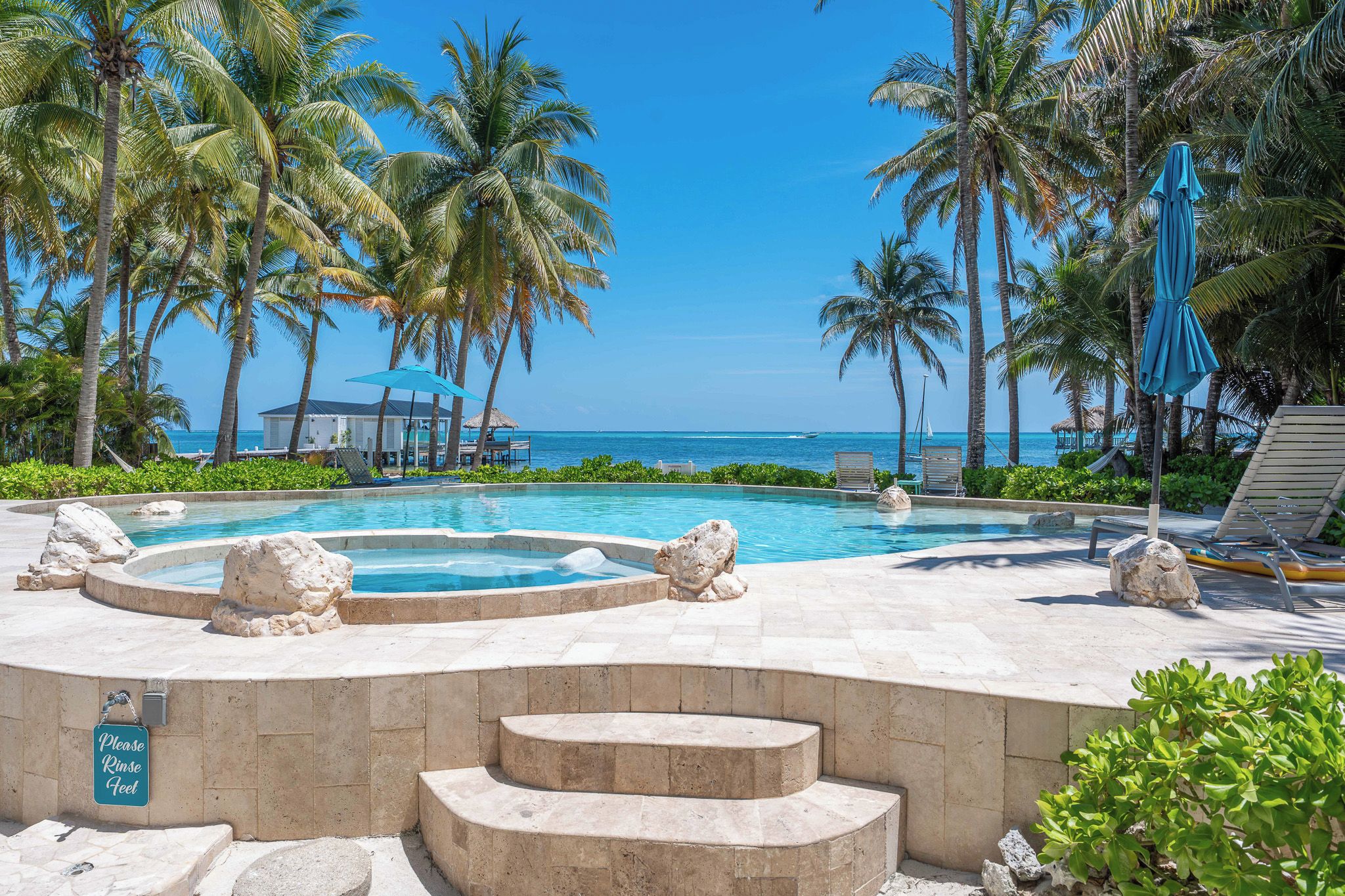 A pool area with a stone border, lounge chairs, and a sign instructing to rinse feet.