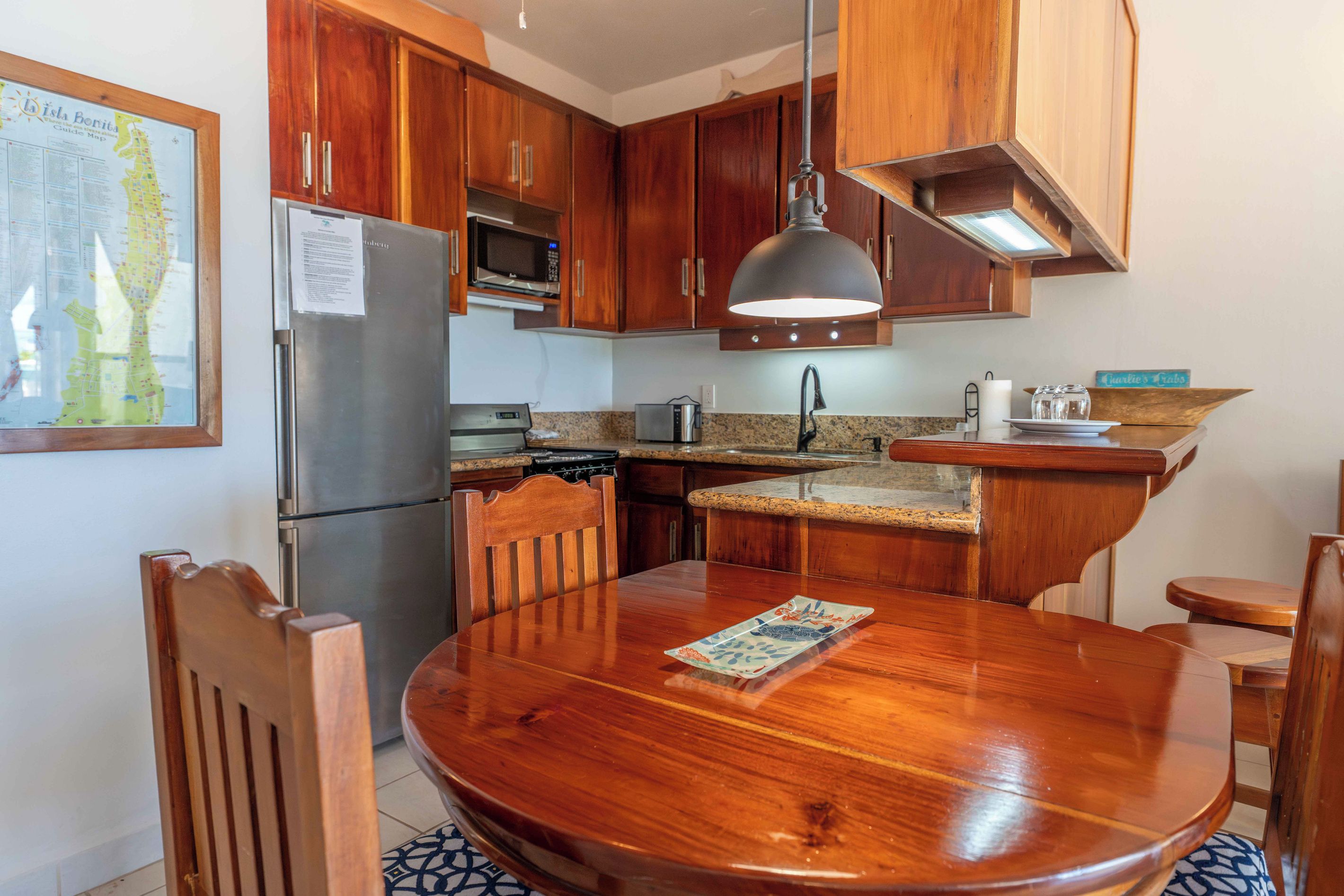 Una cocina con armarios de madera, electrodomésticos de acero inoxidable, una mesa de comedor con sillas y una lámpara colgante.