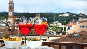 Dos vasos de bebida roja con rodajas de fruta sobre una mesa, con vistas a una torre de reloj y edificios.