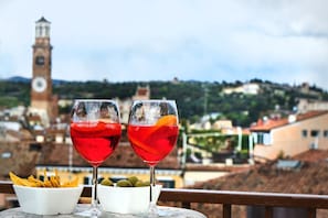 Duas taças de bebida vermelha com fatias de fruta sobre uma mesa, com vista para um campanário e edifícios.