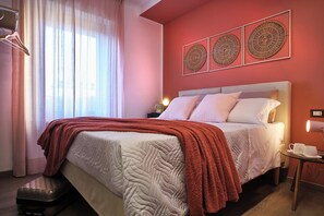 Een hotelkamer met een bed, een nachtkastje, een tafel met kopjes, een raam met gordijnen en wanddecoratie.