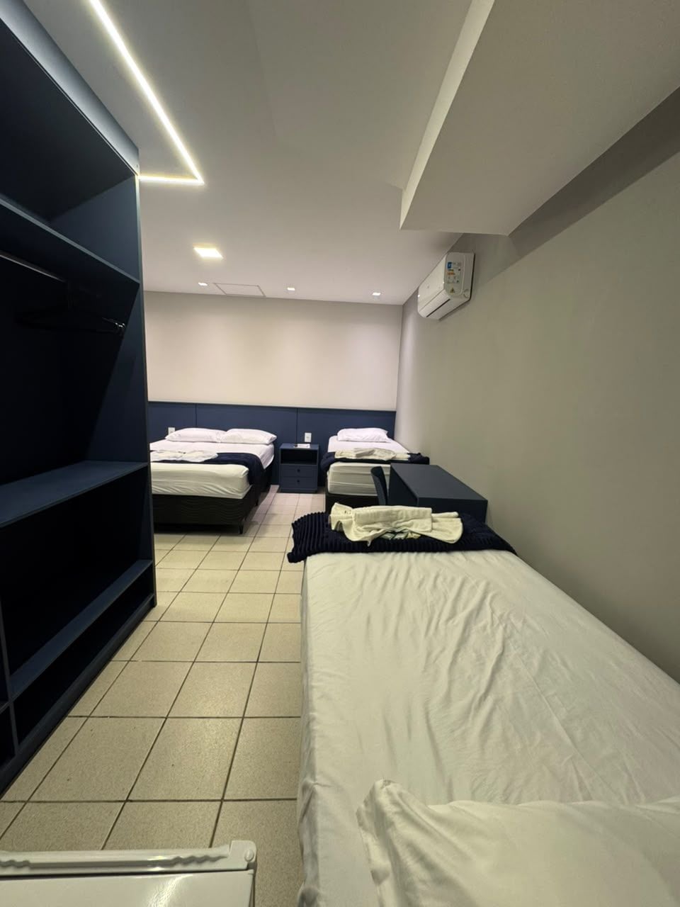 A hotel room with two beds, a wardrobe, and a bedside table.