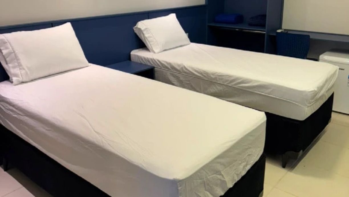 Dos camas individuales con sábanas blancas en una habitación con un detalle en color azul.