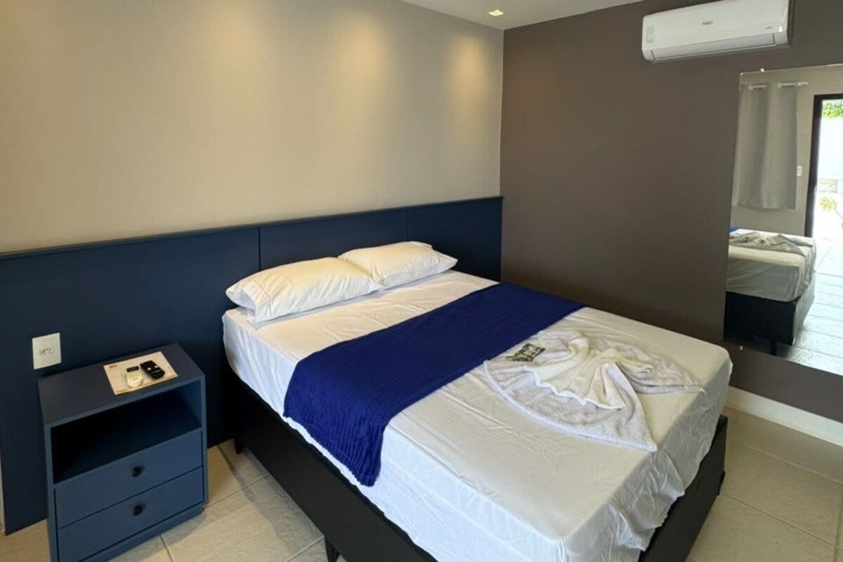 Une chambre d’hôtel moderne équipée d’un lit simple, d’une table de chevet, d’un climatiseur mural et d’une fenêtre avec des rideaux.