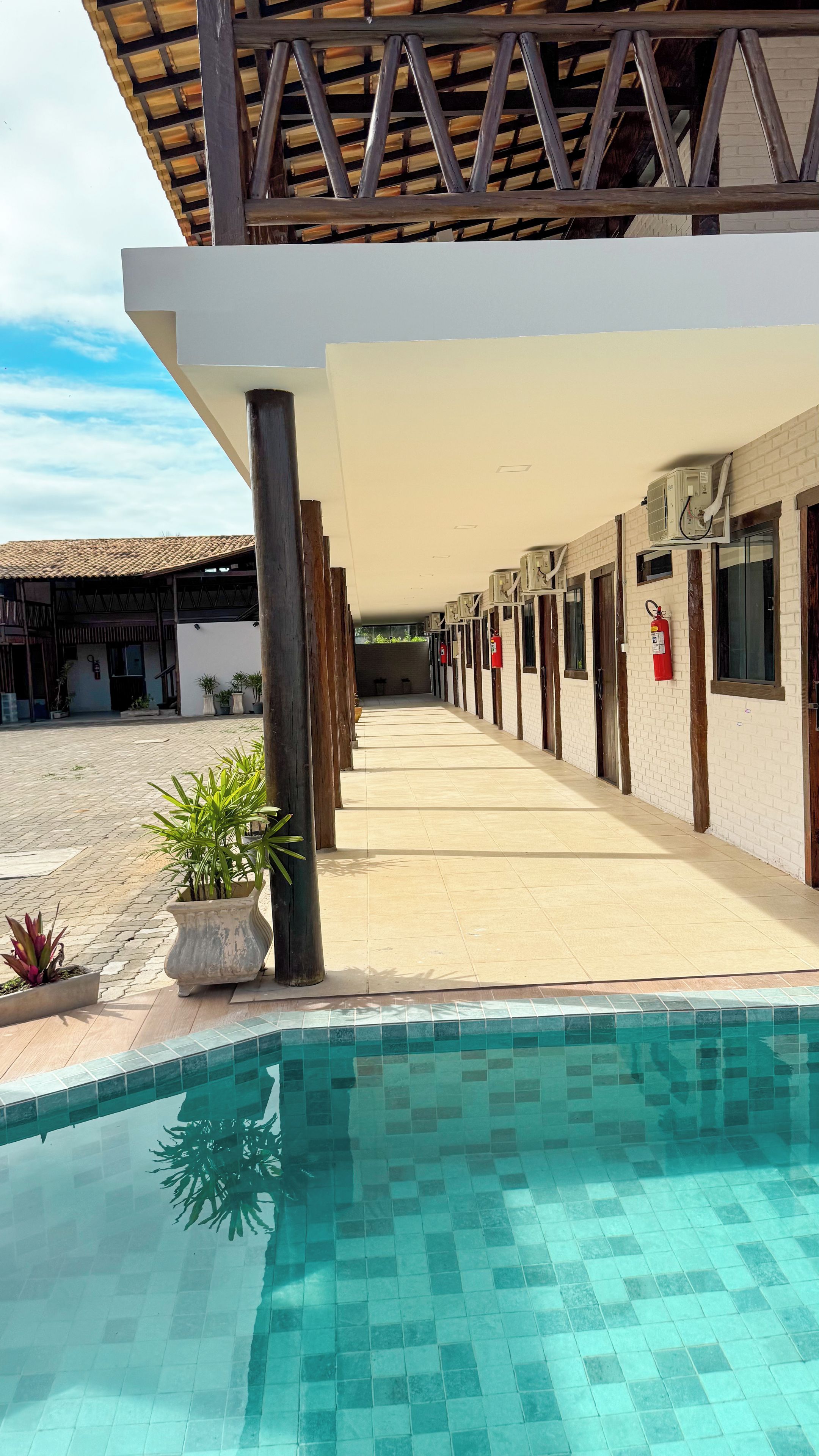 Un área de piscina con suelo de baldosas, un paseo techado y un edificio con ventanas y puertas.