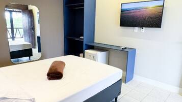 A hotel room with a bed, a desk with a computer, a TV mounted on the wall, and a mirror.