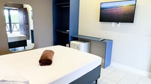 A hotel room with a bed, a desk with a computer, a TV mounted on the wall, and a mirror.