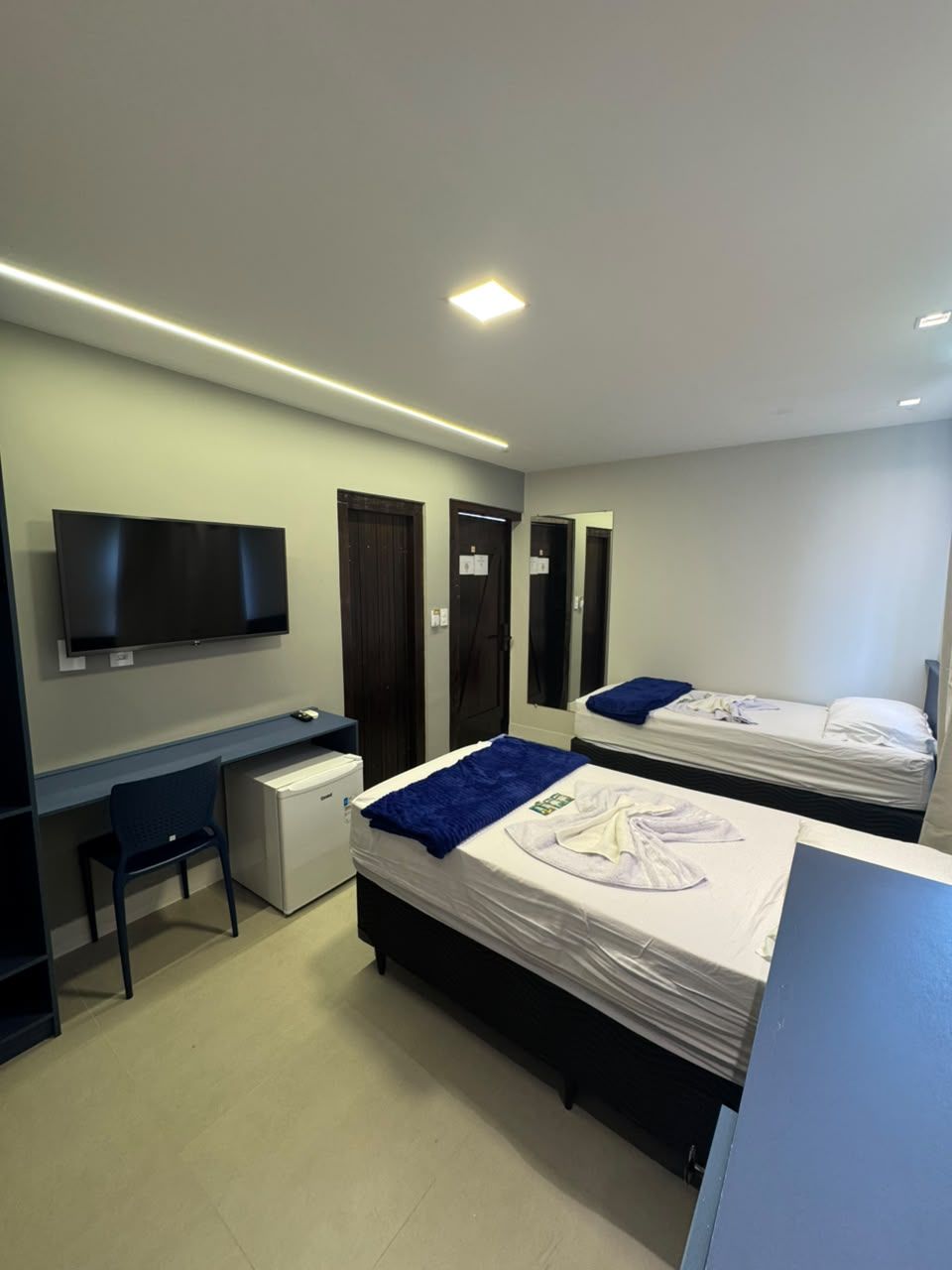 Una habitación de hotel moderna con dos camas, un escritorio, un televisor y un armario.