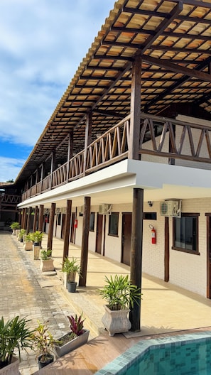 Zona exterior coberta amb piscina, plantes en testos i un edifici amb balcó de fusta.