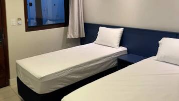 Ett hotellrum med två separata sängar, ett litet bord, ett fönster med gardiner och en dörr.