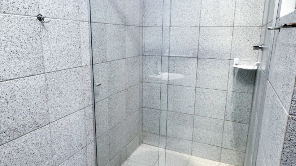 Un vestuario con ducha revestida de azulejos, un lavabo blanco y un perchero.