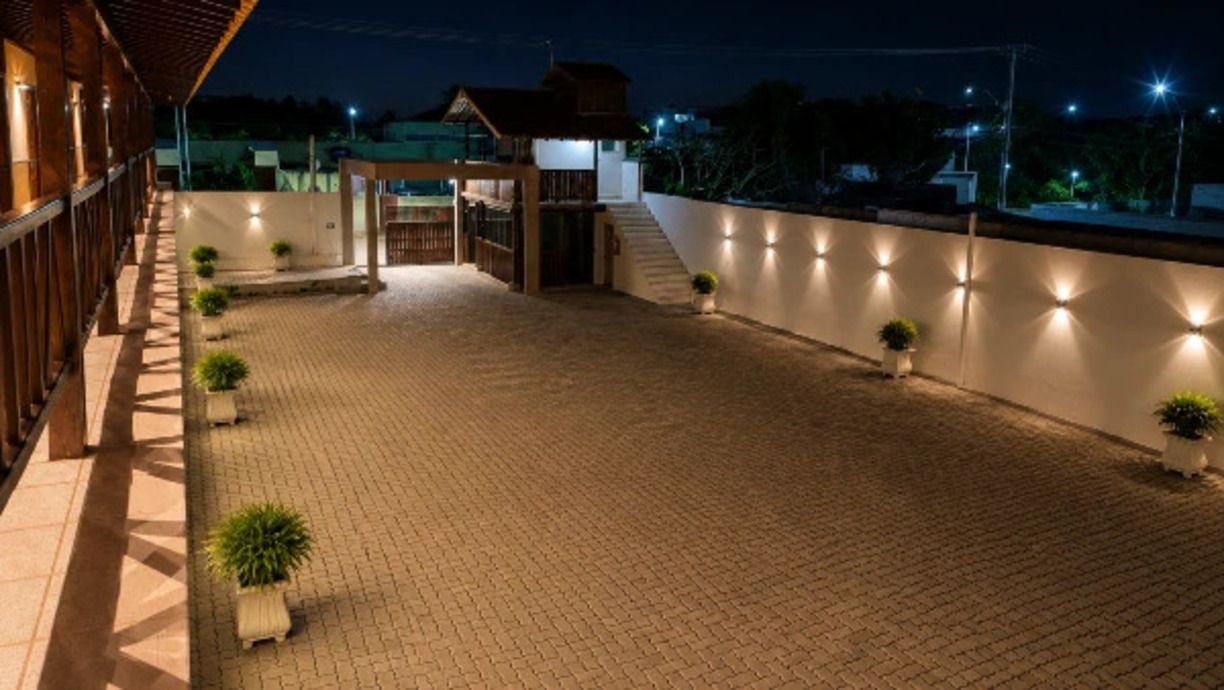 A paved outdoor area with a wooden structure, potted plants, and a wall with lights.