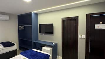 A hotel room with a bed, a desk, a wardrobe, a television, and a door.