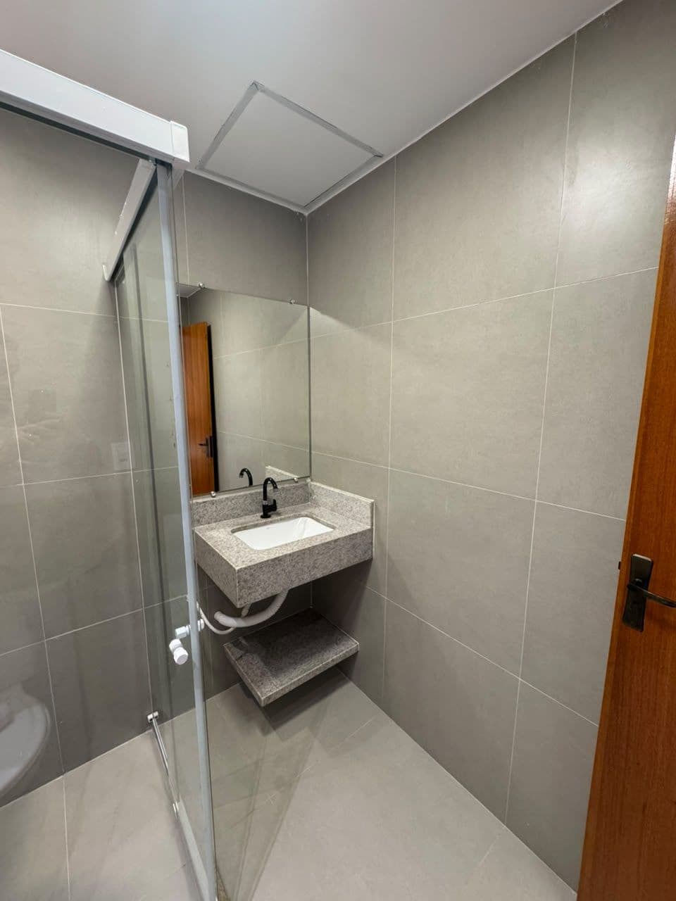 A modern bathroom with a glass shower enclosure, a sink with a mirror, and a wooden door.