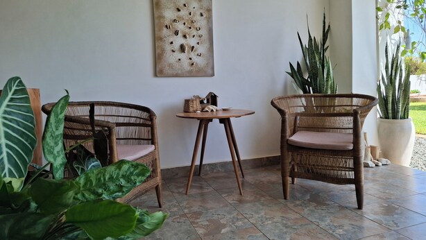 A room with two wicker chairs, a small table, a wall-mounted artwork, and potted plants. - 3 Bed room Beach Bungalow in Dar es Salaam (Dar es Salaam)