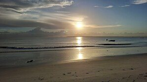 A beach with a calm sea, a boat, and a clear sky. - 3 Bed room Beach Bungalow in Dar es Salaam (Dar es Salaam)