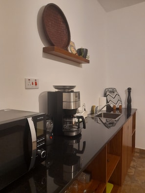 Cozinha com micro-ondas, cafeteira e prateleira sobre o balcão.