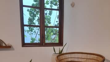 Una stanza con un tavolo in legno, una sedia in vimini, una rivista e una finestra vista alberi.