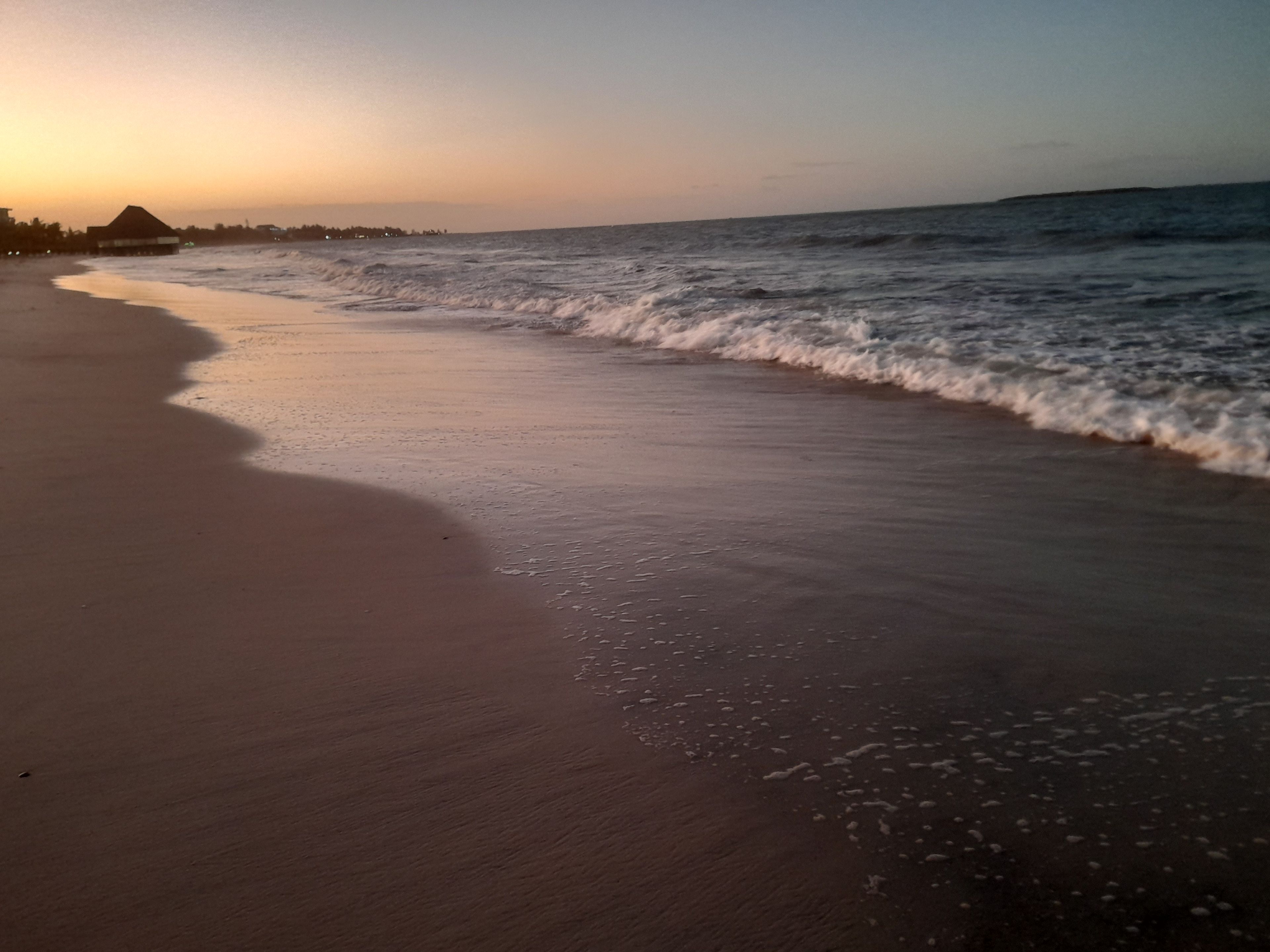 A beach with waves, a structure on the left, and a clear sky.