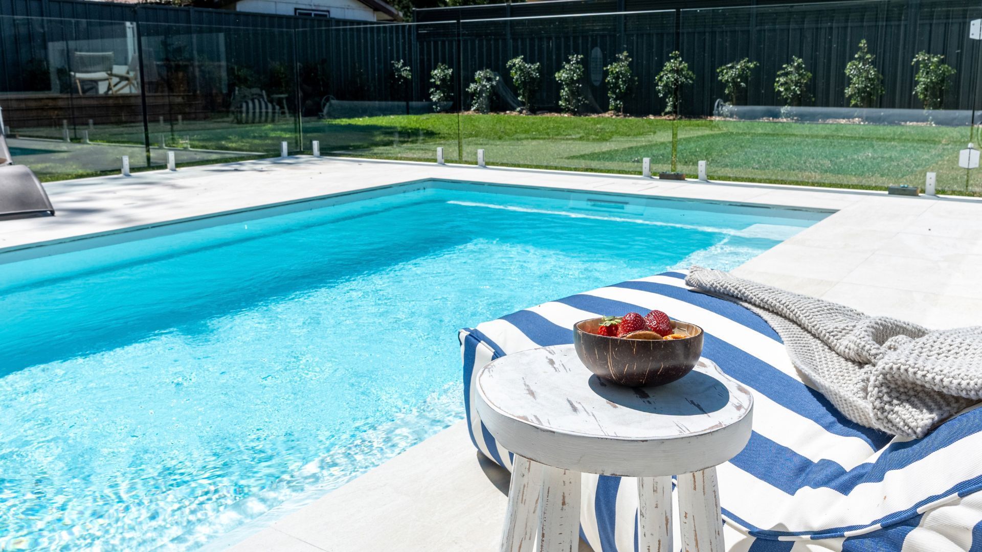 Une piscine avec un fauteuil de relaxation et un saladier rempli de fruits.