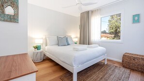 A bedroom with a bed, bedside lamps, a ceiling fan, a window with curtains, and a view of the outside. - Bellaburra – relaxed family beach house near Callala Beach (Callala Beach)