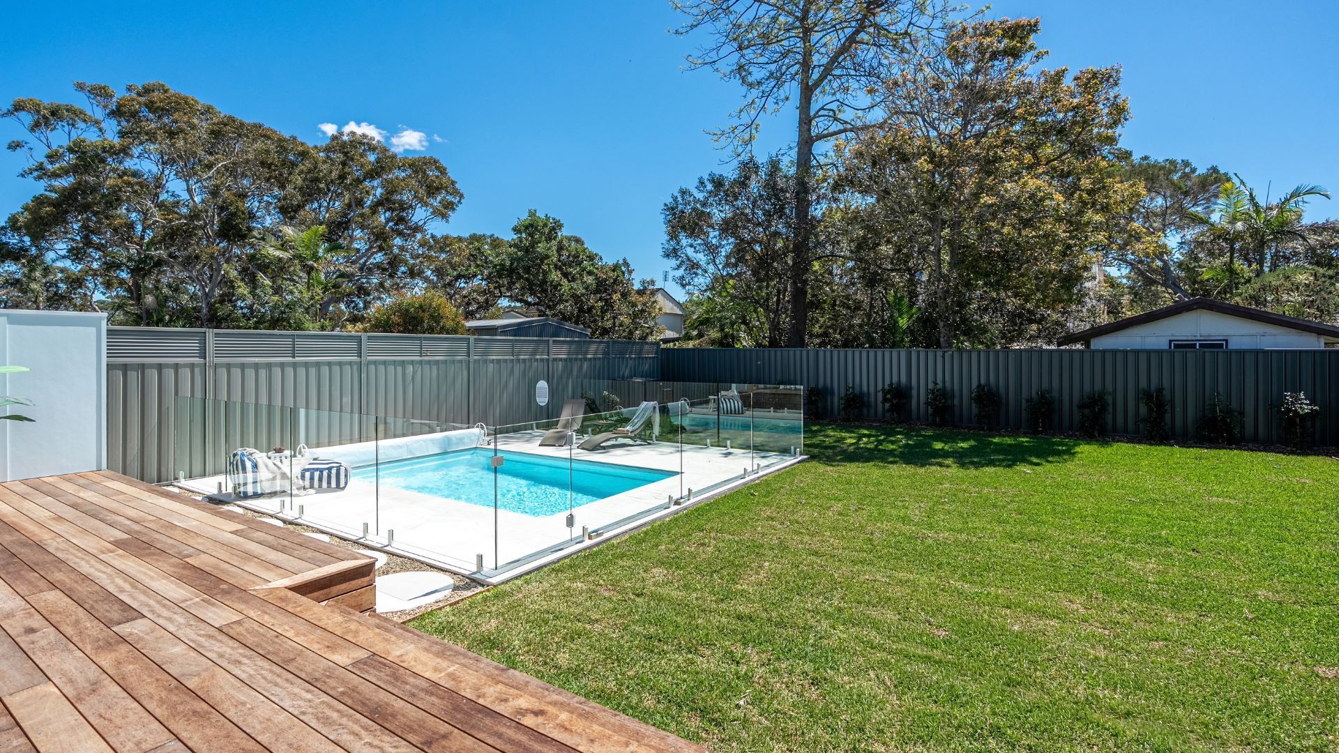 A backyard with a swimming pool, a wooden deck, and a fenced area.