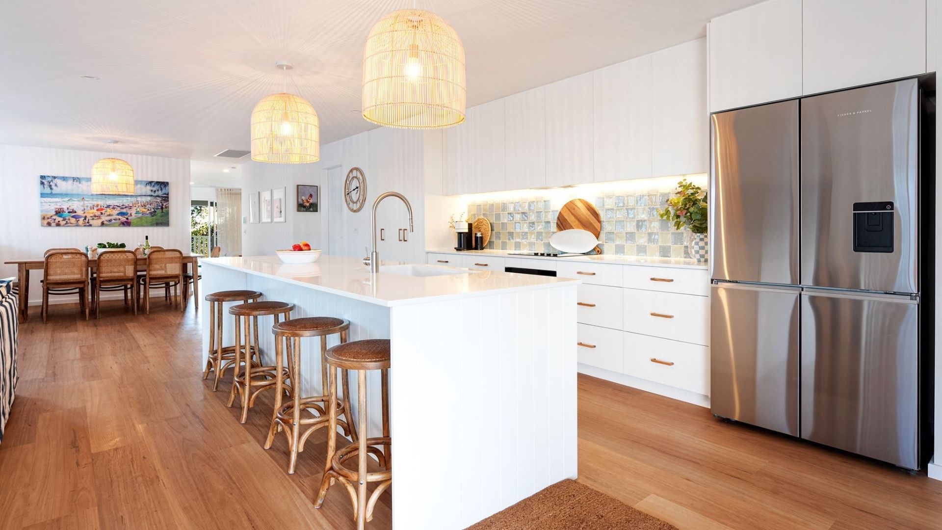 A modern kitchen with a central island, stainless steel appliances, and wicker bar stools.