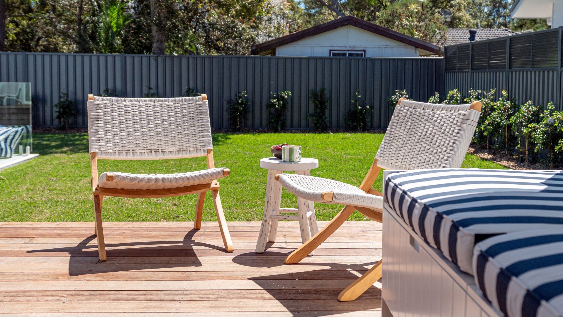 Eine Terrasse mit zwei Korbstühlen, einem kleinen Tisch, einem gestreiften Kissen und einem Haus im Hintergrund.