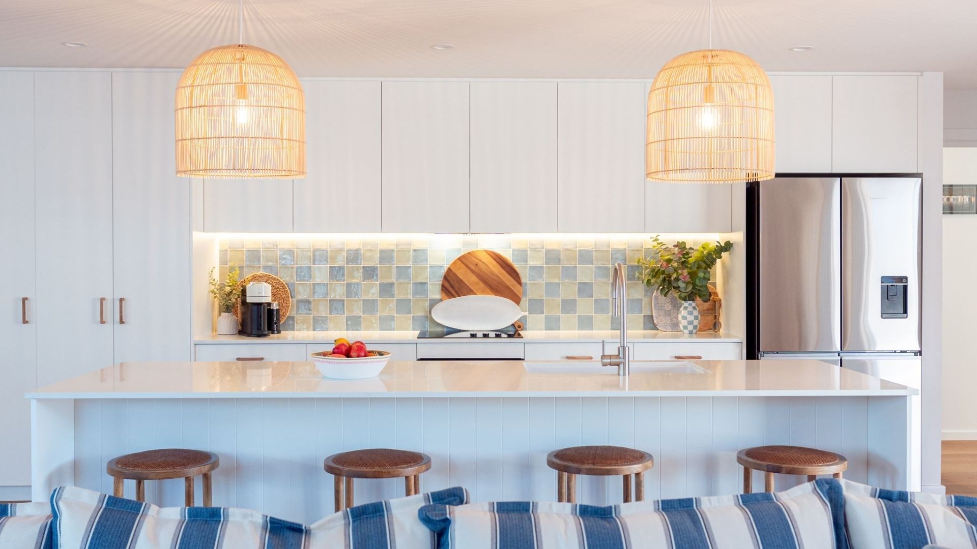 A modern kitchen with white cabinetry, a central island with stools, a stainless steel refrigerator, and two hanging pendant lights.